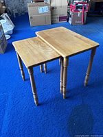 Two wooden side tables positioned fitted under one another on blue carpet floor