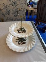 Two-tier ceramic plate set shown assembled, depicting Christmas tree and present designs on white ceramic plates with gold accents.