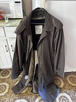 Full view of the brown men's trench coat showing its length, collar, and shoulder epaulets.