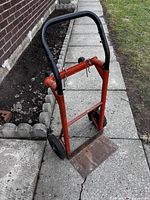 Front angled view showing red metal frame, black handle, wheels and rust on flat base plate