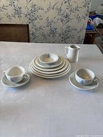 Table setup showing all plates, two small bowls, two mugs, and one creamer jug with floral wallpaper background.