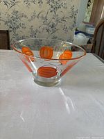 Side view of clear glass bowl with orange leaf design on a white tablecloth and floral wallpaper background.