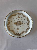 Top-down photo of round porcelain tray showing the delicate hand-painted gold floral design scattered across the surface and scalloped gold rim.