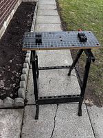 Photo of the portable work bench standing on a concrete path near a garden bed.