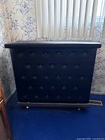 Front view of retro bar showing black tufted padded front panel with button details and chrome footrest bar.