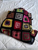Crochet blanket folded showing colorful granny squares bordered in black yarn.