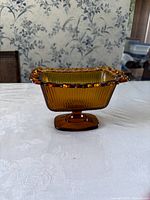 Side view of amber glass candy dish showing ribbed pattern and pedestal base.