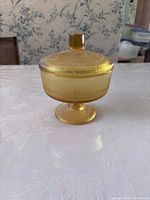 Front side view of the yellow glass container with the lid on, showing the textured pattern, pedestal base, and knob handle on the lid.