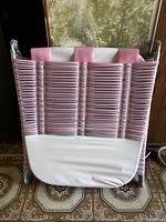 Folded sun lounger showing the pink and white woven straps and metal frame.