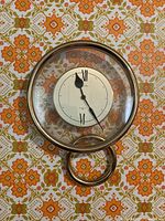 Front view of the Seiko wall clock showing the round face, Roman numerals XII and VI, and gold-tone outer frame with a circular ring accent below.