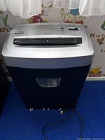 View of front side of Fellow's paper shredder showing paper slot, control switch, and power cord on floor.