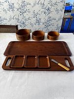 Photo showing entire set of wooden trays and bowls on a white tablecloth with a floral wallpaper background
