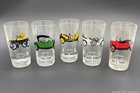 Image of five collectible cocktail glasses each with vintage car illustrations and model year text: Studebaker Electric 1902 in yellow, REO 1913 in green, 1912 Hudson in yellow, Nash Rambler 1909 in black and white, and Ford 1924 in red.