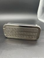 Side view of antique Rolls razor metal case showing engraved Greek key pattern and circular razor blade logo.