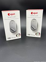 Two boxed August Smart Lock units model ASL-3B showing front packaging with lock image and keyless entry features.