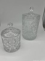 Two crystal biscuit barrels with lids, one large and one smaller, showing intricate cut crystal designs.