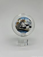 Front view of glass paperweight showing a panda lying on a landscape with flowers and Chinese characters