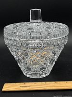 Front angle view of vintage clear glass covered candy dish showing intricate cut pattern, faceted knob lid handle, and approximately 7 inch height next to ruler.