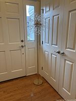 Full view of the gold metal floor lamp showing the base, pole, and closed door background