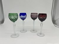 Front view showing 4 different colored Bohemian Czech cut crystal wine hack glasses with intricate cut patterns and clear stems.
