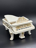 Front side close-up of the off-white ceramic piano-shaped trinket box with gold accents and hand-painted keyboard detail.