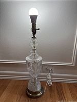 Front view of the crystal and metal table lamp illuminated showing clear intricate cut crystal body and gold-tone base.