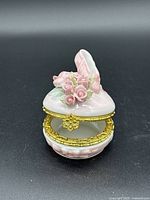 Porcelain music box shaped like a ballet slipper adorned with pink roses and gold metal trim. Shown closed with clasp view.