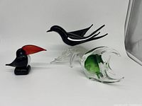 Full view of three glass animal sculptures including black bird, toucan, and fish