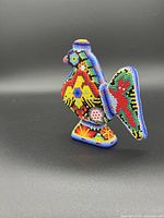 Side angled view showing detailed multicolored beaded pattern on wooden bird figurine.