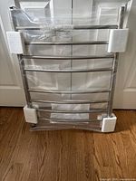 Heated towel rack wrapped in plastic with foam corner protectors, showing curved horizontal bars and overall rack structure.