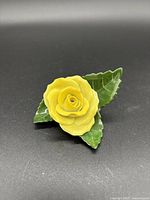 Handpainted porcelain figurine of a yellow rose flower with two attached green leaves, detailed with leaf veins.
