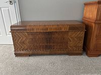 Front view of the closed cedar hope chest showing decorative wood veneer and carved feet.