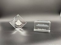 Photo showing two glass paperweights on a gray background: the Queen Mary 2 etched in a rectangular block, and the Lorenzo tall ship in a diamond-shaped block.