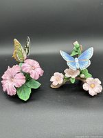 Front view of two porcelain figurines featuring butterflies and flowers on black background.