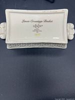 Photo of basket bottom showing Lenox Crossings Basket stamp, gold logo, and embossed pattern on white ceramic.