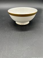 White porcelain fruit/dessert bowl with gold ornate band on rim against a dark background.