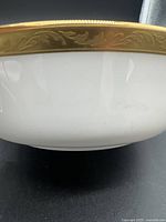 Close-up view of gold rim showing detailed embossed leaf or scroll pattern on white porcelain bowl.