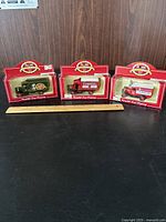 Lot of 3 Lledo diecast Campbell's Soup 100th anniversary model delivery trucks in original red branded packaging on black surface with wooden ruler.