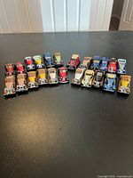 Wide view of all 23 toy cars arranged on a black surface showcasing various colors and models.