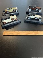 Four Solido 1:43 scale model cars displayed on black bases with model names and numbers visible, arranged on dark surface next to a ruler for scale reference.