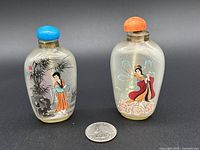 Front and side view of two glass snuff bottles with traditional Chinese paintings and colored tops, shown with coin for scale