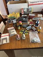 Overview of N gauge model train buildings and accessories spread on wooden table including original boxes and plastic packaged parts