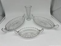 Three clear glass Fostoria Cubist relish trays along with one matching vase displayed on a flat surface.
