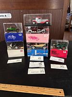 Lot of 6 Rio model cars displayed in clear cases with original boxes beneath and beside each, placed on black surface with ruler for scale.