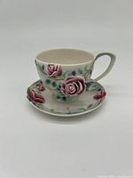 Front view of the porcelain teacup and saucer, showing raised pink rose decoration and floral patterns.