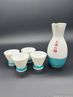 Full set of one ceramic sake carafe and four matching cups against black background.