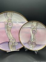 Set of two Frederick Frances porcelain plates on display stands, showing the artistic abstract design and gold trim edges