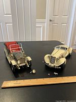 Two vintage toy cars on a black surface, showing detached parts in front.