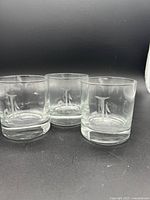 Set of three clear old fashioned glasses with etched letter 'J' on each glass, shown against black background.