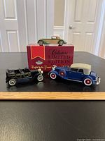 Three toy cars displayed on a table with a ruler for scale; one car is positioned on its original Limited Edition box.